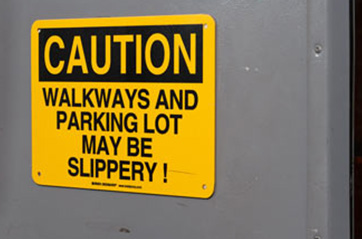 A sign that says "CAUTION WALKWAYS AND PARKING LOT MAY BE SLIPPERY."
