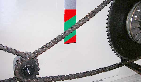 A machine with a chain connecting two gears. The center of the chain is in line with a section of green marked behind it, indicating its optimal tightness.