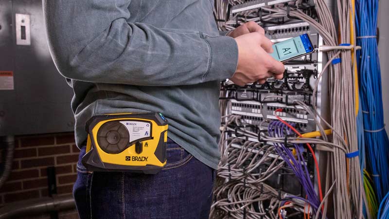 A worker creates a wire and cable label on an app for a portable label printer in a server room setting.