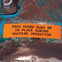 A label firmly adhered to a rusted metal container outdoors.