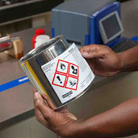 A person applying a hazardous materials label to metal can.