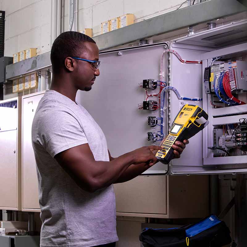 An electrician works on labeling components of an electrical panel.