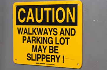 A bright yellow sign on a door warning that walkways may be slippery.
