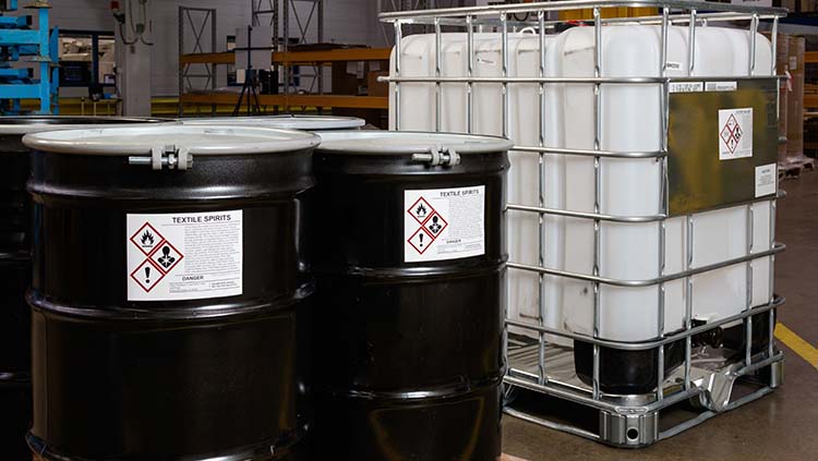 Chemical drums and containers with GHS labels used as primary containers in a warehouse setting.
