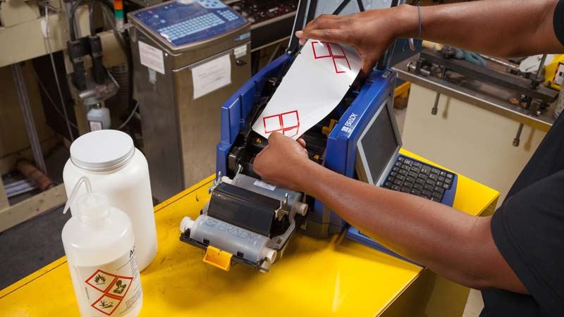 An industrial worker creates HazCom labels to put on secondary containers in a warehouse setting.