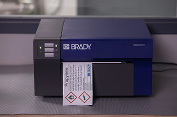 A Brady BradyJet J4000 sitting on a felt pad on top of a table in the process of printing a label.