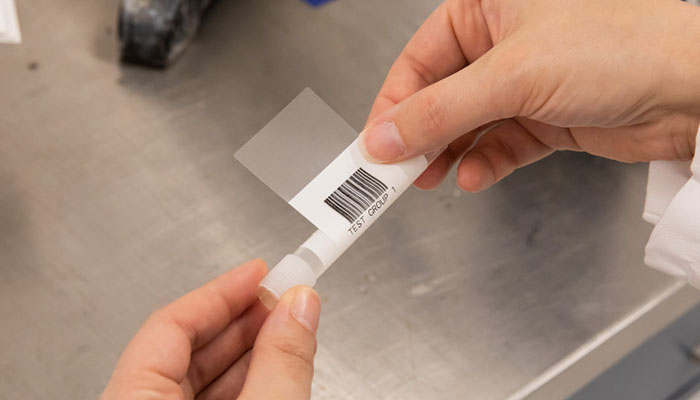 A scientist applying a barcode test tube label coated in acrylic-based adhesive.