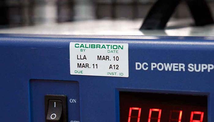 A DC power supply reading 0.018 with a calibration label depicting the due date for the next inspection.
