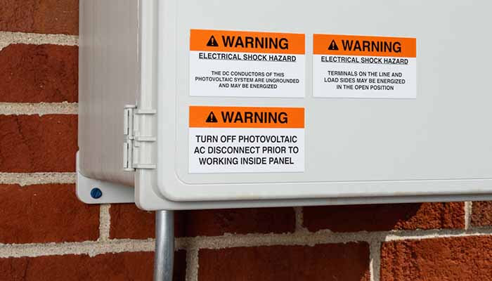 Close up of an electrical panel with 3 acrylic-based adhesive warning labels attached to the front.
