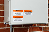An outdoor electrical box with warning labels.