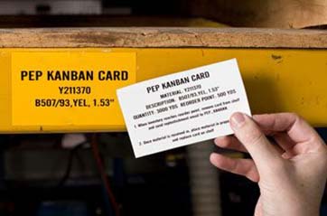 A person holds up a Lean/5S card to its matching label on a shelf.
