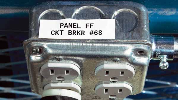 A label on an outlet panel. The top of the panel has an irregular surface as opposed to a flat one, but the label is still firmly adhering to it.