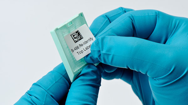 A person with chemical-resistant gloves is applying a label to a small piece of equipment.