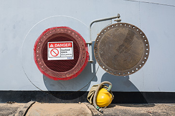 A confined space cover and sign warns workers of dangers and accessibility.