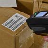 A scanner reading a barcode label on a shipping box.