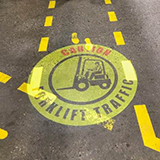 A caution forklift traffic sign projected onto a walkway within a manufacturing environment.