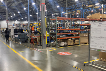 A worker marking an area of a manufacturing facility with yellow and black striped tape.