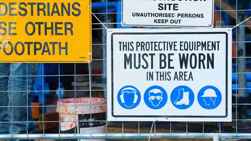 A fence with a sign that says 'protective equipment must be worn in this area.'