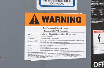 A bright orange arc flash warning label on the outside of an electrical panel.