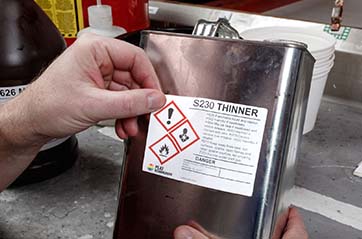 A person applies a HazCom label to a can of thinner.