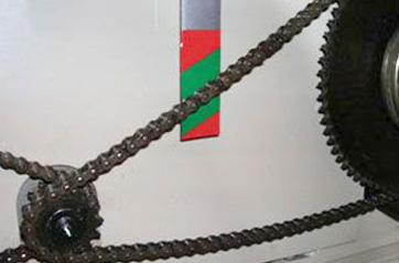 A chain connecting two gears. There is a label behind the chain with a green area indicating how much slack the chain should have.