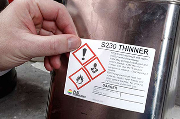 A person applying a HazCom label to a container of thinner.