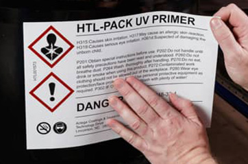A person attaching a hazard label to a barrel.