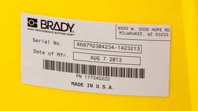 A Brady glossy metallized polyester label applied to the curved surface of a larger cannister.