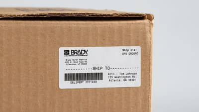 A Brady paper shipping label applied to cardboard shipping box.