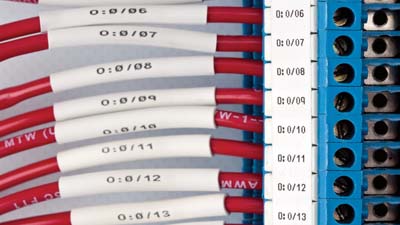 A series of red cables with heat shrink identification sleeves within a terminal block.
