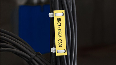 A yellow cable tag zip tied to a black cable within a bundle of cables.