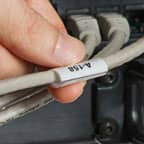 A person holding a wrap-around label applied to a gray cable.
