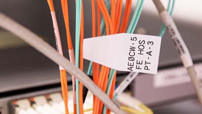 A Brady quick flag label extending from a cable, amongst a larger group of labels, with printed text to identify it.