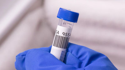 A laboratory technician holding a test tube with a Brady cryogenic polyester label applied to it. The label has both text and a barcode printed on it.