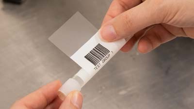 A Brady self-laminating polyester label with a barcode printed on it being wrapped around a test tube.