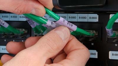 A self-laminating vinyl wrap-around label being wrapped around a green Cat-5e cable.