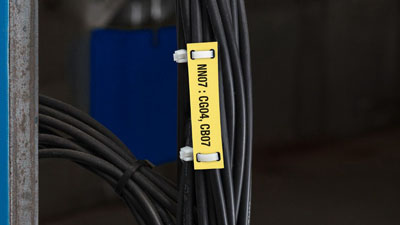 A yellow tear-resistant tag with printed black text attached to wire that is part of a larger bundle of wires.