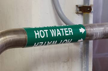 A hot water pipe marker identifying the contents and flow direction of an industrial pipe.