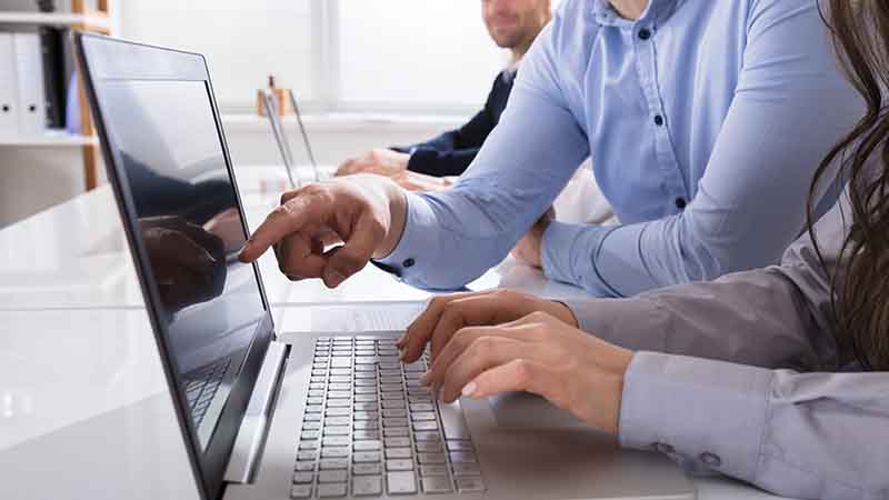 A man works on a laptop in a busy office.