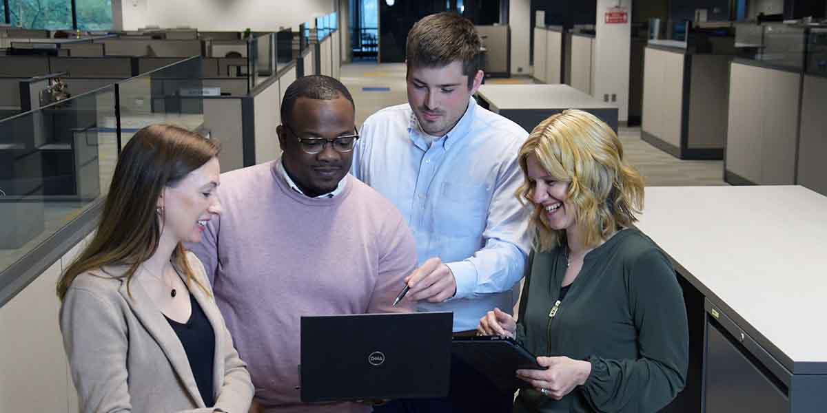 Four workers looking at a laptop screen. They seem happy and relaxed.