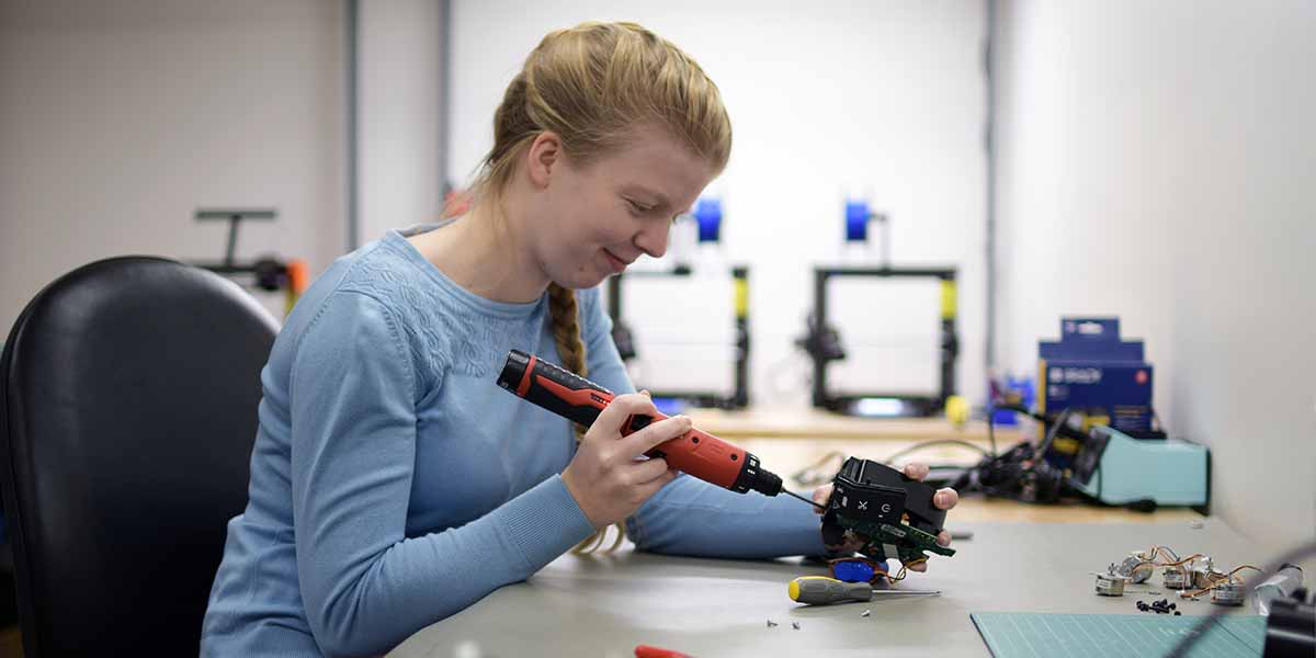 A woman in an engineering lab smiling as she adjusts a small mechanical component.
