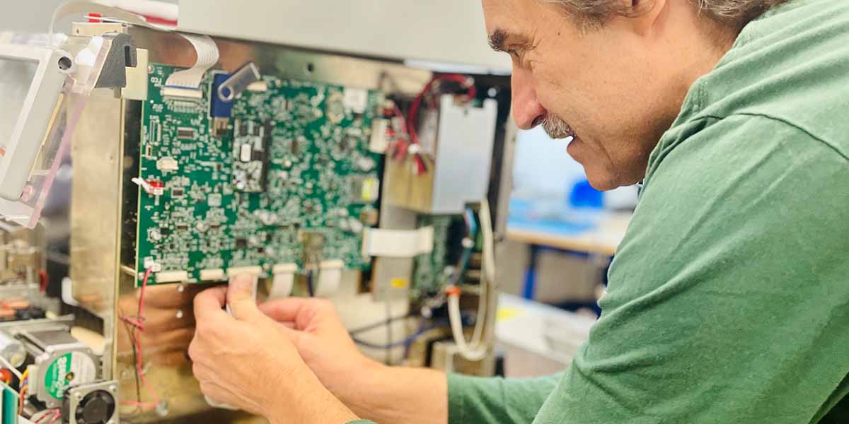 A member of Brady's service team is intensely focused on repairing a circuit board.