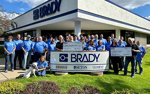 A group of employees posing outside their building with an oversized charity check.